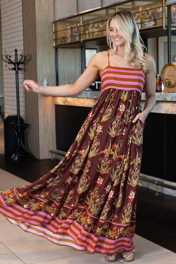 maxi dress with a brown base, pink and orange horizontal stripes on the bodice and hem, and a botanical print in gold, green, and orange across the skirt